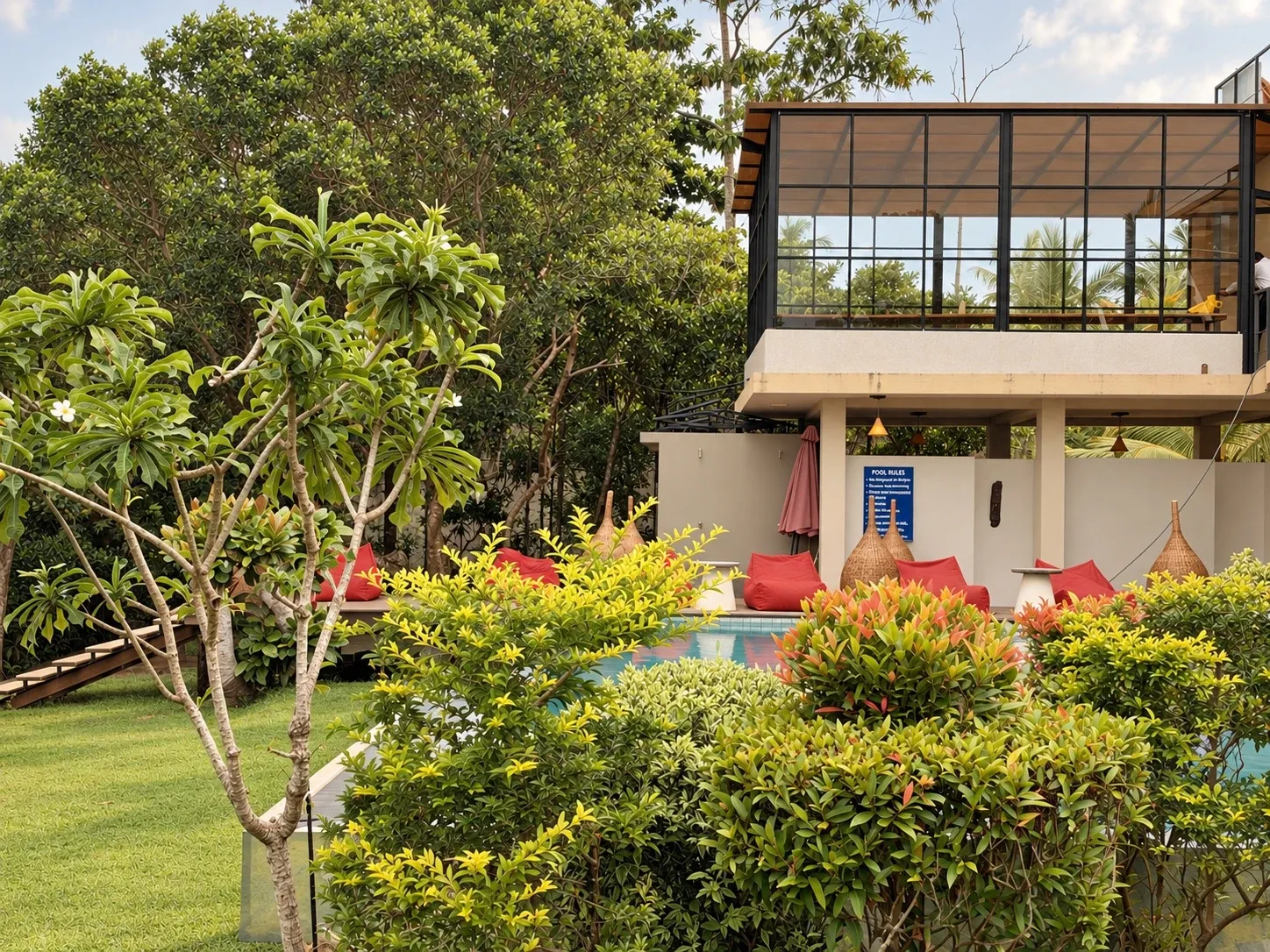 A glass-walled room on the upper floor above the poolside lounge, with red beanbags and flowering shrubs in the garden