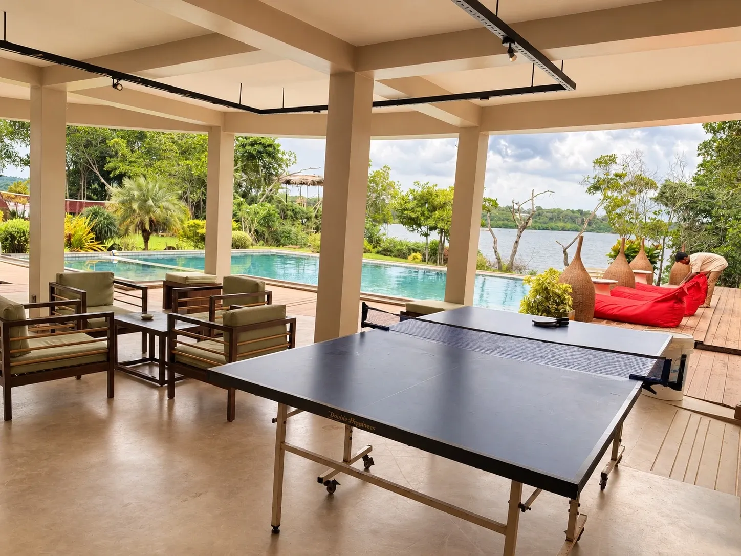A table tennis table and armchairs in the open lounge beside the pool, with the lake behind