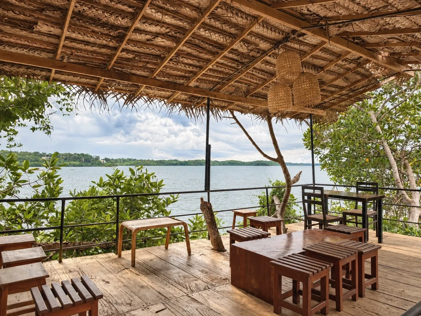 A thatched deck above the lake, with timber tables and stools and woven lamps