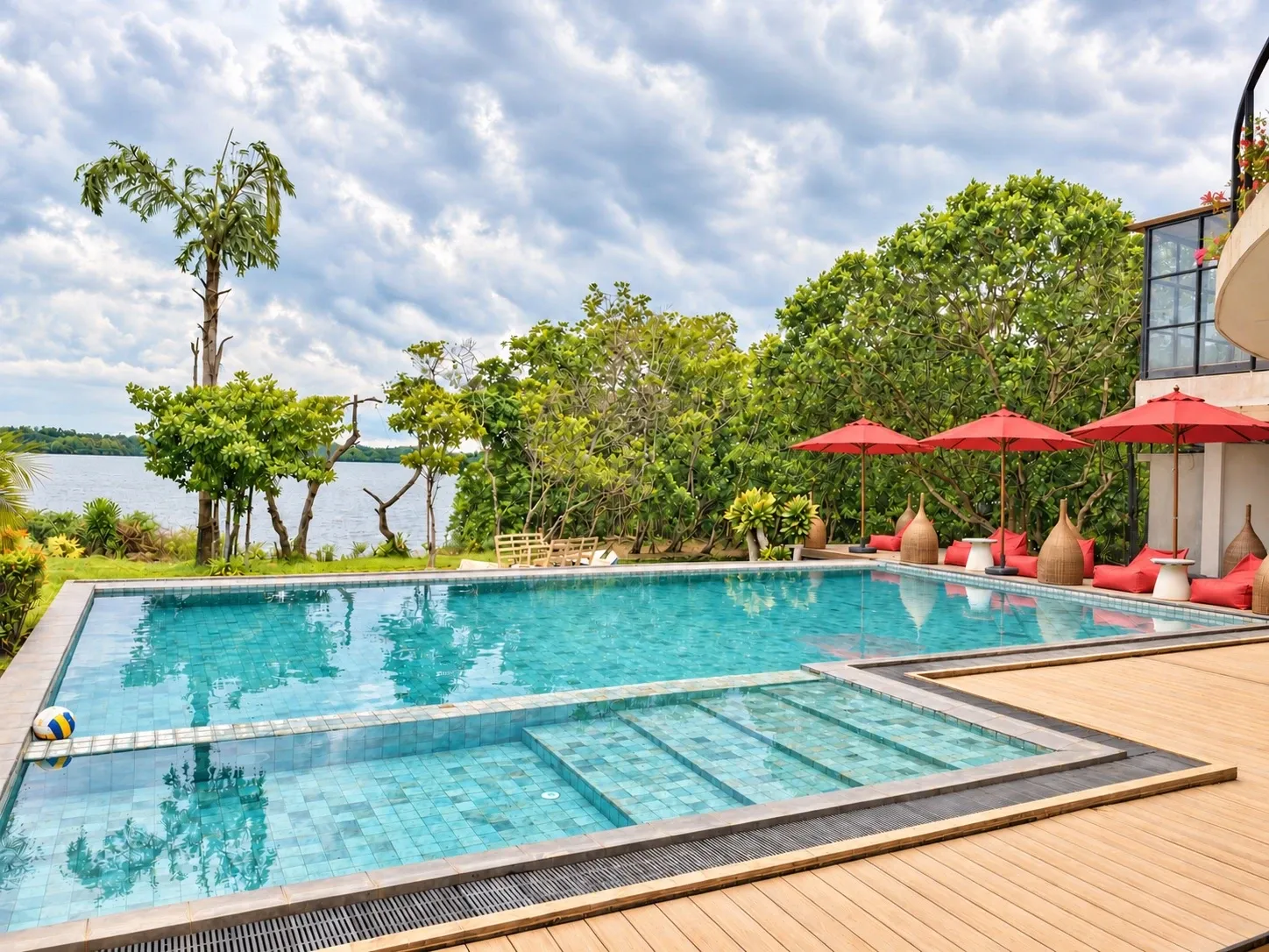 The pool, with red umbrellas and beanbags along the far side and the lake behind
