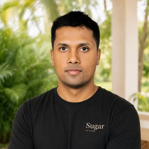 Saliya in a black Sugar co-living T-shirt, with palm trees behind him